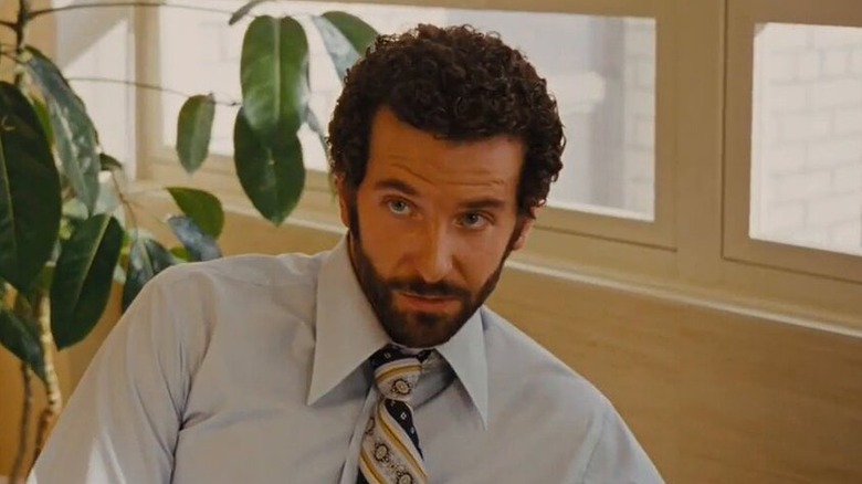 Bradley Cooper ca Richie DiMaso așezat în fața unei fabrici din American Hustle