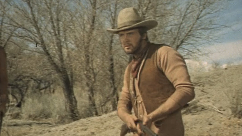 Lee Majors' Blue traversează câmpiile ținând o pușcă în Will Penny