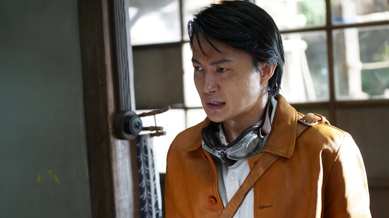 Ryûnosuke Kamiki în rolul lui Kôichi Shikishima în picioare lângă o uşă cu ochelari de protecţie la gât în ​​Godzilla Minus Zero
