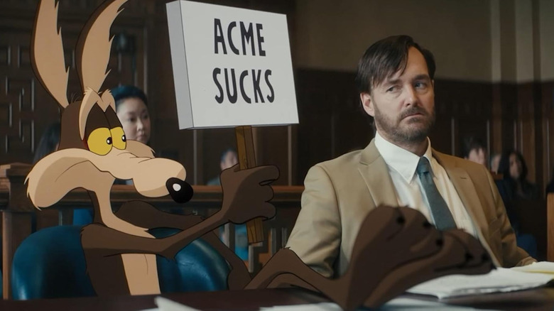 Wile E. Coyote ridică un pancart pe care scrie „Acme sucks” lângă Will Forte în rolul lui Kevin Avery în Coyote vs. Acme