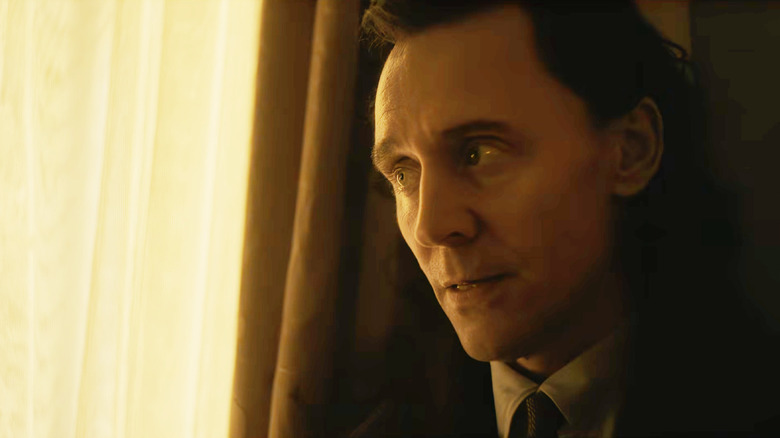 Tom Hiddleston în rolul lui Loki purtând un costum și stând lângă draperiile ferestrelor în Avengers: Doomsday