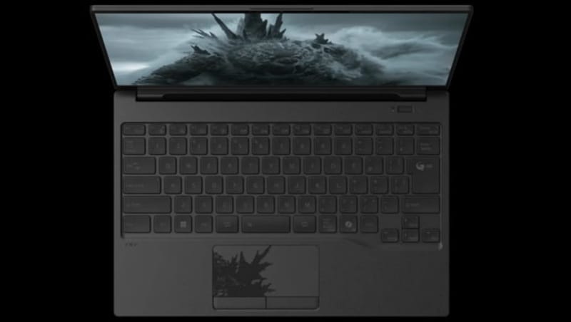 Capac pentru laptop Fujitsu Godzilla care arată o ilustrație Godzilla neagră și touchpad în formă de aripioară dorsală